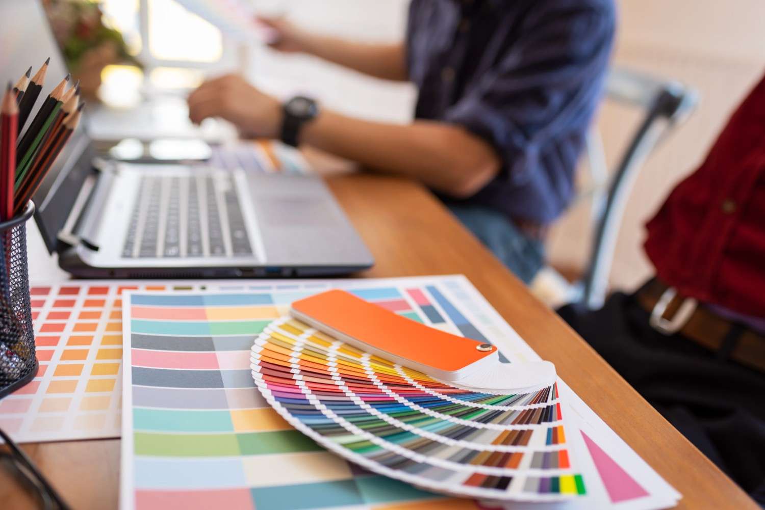 Color swatches spread on a desk with a notebook and laptop in a bright workspace.